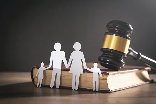 paper cut out of a family leaning against a law book and gavel.