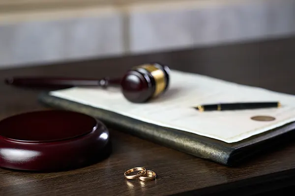 two wedding rings on a desk in front of a legal pad, pen and gavel.