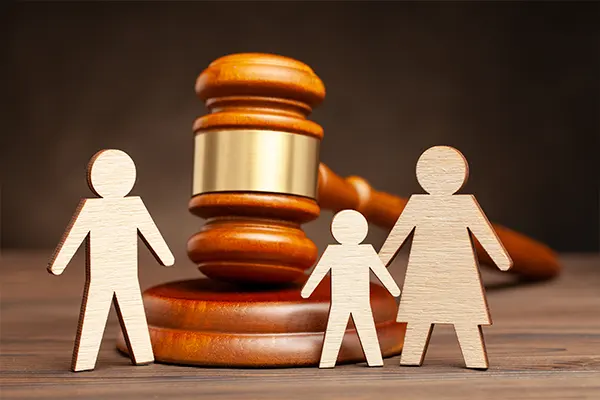 paper cutouts of two parents being separated by a gavel with a child holding the hand of one parent.